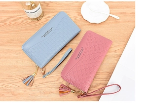 Close-up of long zip wallets with bow embossing, tassels and wristlet on wood table