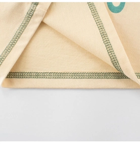 Détail de l'ourlet d'un t-shirt beige clair avec coutures contrastées vertes à double aiguille