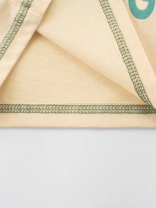 Détail de l'ourlet du T-shirt enfant crème avec surpiqûres vertes contrastées