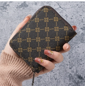Detail view of a dark brown compact zip wallet with golden floral patterns in hand