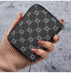 Close-up of a black pebbled leather card holder with monogram patterns and metal zipper