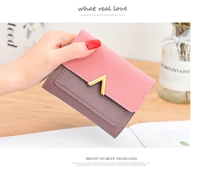 Detail of female hand holding a small bifold wallet with V-shaped metal buckle in pink and purple