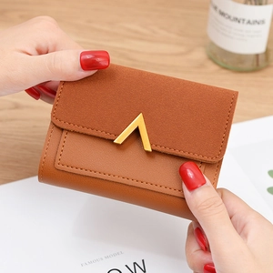 Brown leather bi-fold wallet with gold V-shaped buckle held against a lifestyle background