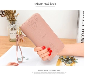 Close-up of pink long wallet with leaf embossing, tassel charm and wrist strap