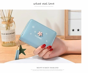 Close-up of light blue floral wallet with tassel zipper and pink flower buckle detail