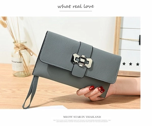 Detailed view of grey litchi grain leather clutch with silver metal clasp on a wooden desk