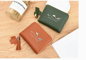Detail shot of forest green and brown wallets with metal dolphin and clover tassel