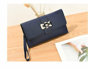 Detail of navy blue lychee pattern leather clutch with silver bow clasp on wood surface