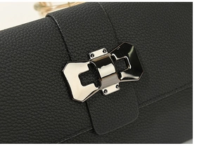 Detail of black lychee grain leather crossbody bag with metal bow lock and fine stitching