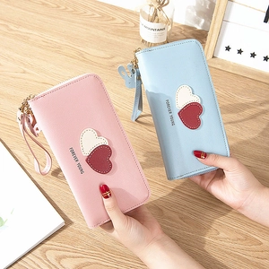 Pink and blue long leather zip wallets with heart patches on a wooden background