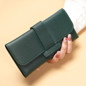 Detail of dark green textured leather long wallet showing flap cover and strap closure