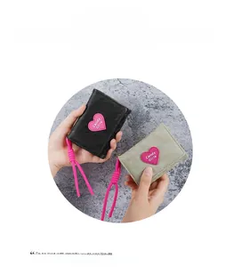 Detail of minimalist leather wallet featuring pink heart patch and woven strap detail