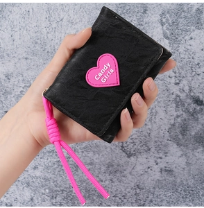 Close-up of black wrinkled wallet with pink heart patch and woven strap in hand