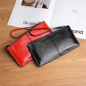 Minimalist long zip wallet in red and black leather with wrist strap on a wooden table