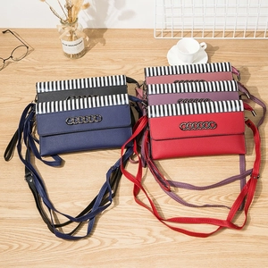 Multiple colors of striped crossbody cell phone bags on a wooden desk with lifestyle props