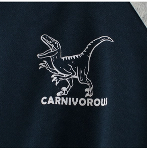 Detailed close-up of navy knit sweatshirt with white dinosaur print and CARNIVOROUS text