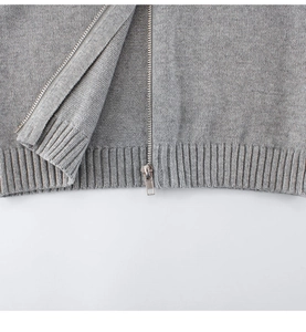 Close-up of gray knit cardigan featuring fine texture, metal zipper and ribbed hem details