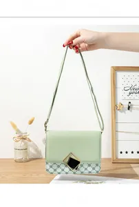 Detail of light green leather crossbody bag with black and white logo pattern and gold buckle