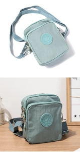 Detail of a sage green nylon crossbody bag showing smooth texture and round logo emblem