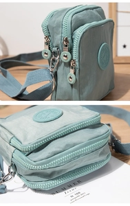 Detail view of mint green nylon crossbody bag with three zipper compartments and logo