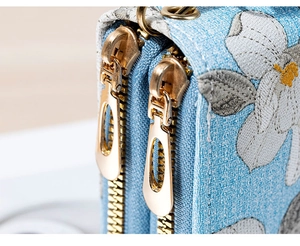Close-up of double metal zippers and floral embroidery on a light blue fabric bag