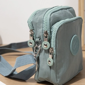Three-layer light green crossbody bag in durable nylon with multi-zipper compartments