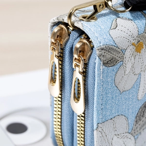Light blue fabric wallet with double gold zippers and delicate white floral embroidery
