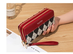 Detail of red and checkerboard double zipper wallet held in hand over a wooden desk