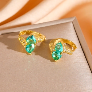 Macro detail of gold-tone emerald huggie earrings with pear-cut green stones and small diamonds