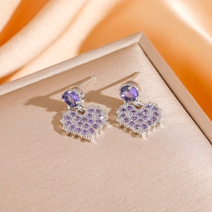 Detailed close-up of purple heart-shaped drop earrings set on a silk background