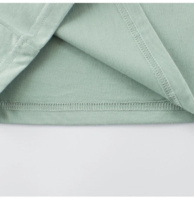 Detail van dubbele naaldstiksels en katoentextuur op de zoom van lichtgroen t-shirt