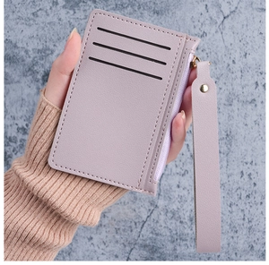 Detailed view of lilac leather card holder with zip pocket and wrist strap held by hand