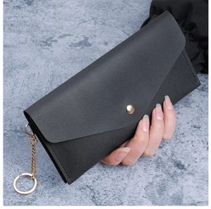 Detail of black leather envelope wallet featuring a gold snap button and metal chain strap