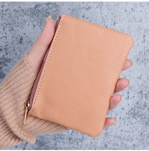 Close-up of pebble grain leather mini wallet with gold zipper detail held by a person