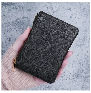 Close-up of minimalist black lychee grain leather mini wallet with gold zipper detail