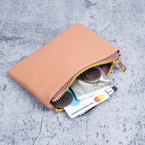 Compact orange-pink lychee grain leather wallet with gold zipper on marble background