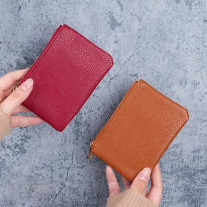 Compact lychee leather coin purses in red and tan with gold zippers shown on stone background