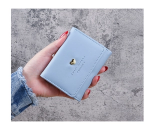 Close-up of light blue leather wallet with heart metal detail held by a model