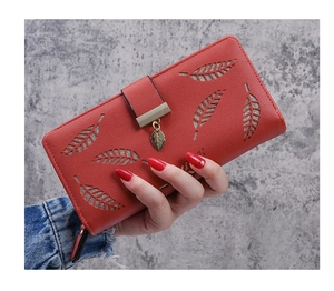 Detail of red long purse featuring a leaf cutout design and golden leaf pendant charm