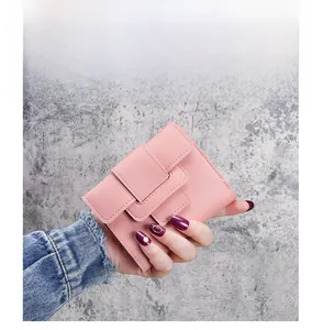 Close-up of a pale pink leather tri-fold wallet with a wide strap buckle closure detail