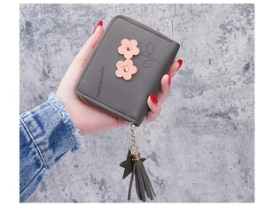 Detail of dark grey short zip wallet with floral charms and tassel in model's hand