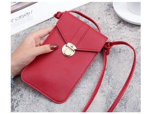 Detailed view of red textured leather crossbody phone bag with gold metal clasp on a desk