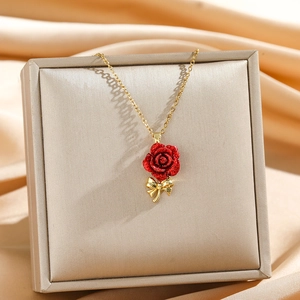 Elegant gold necklace featuring a sparkling red rose pendant with a petite golden bow