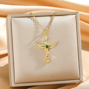 Golden wing cross necklace with emerald green stone and snake wrapping on satin background