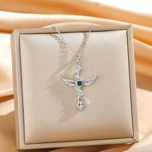 Silver cross wing necklace with green square zircon stone on silk fabric background