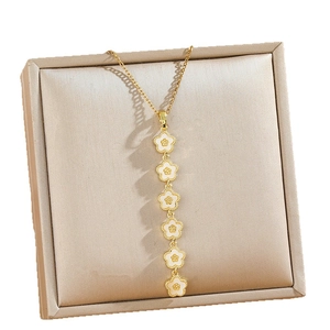 Long collier à pompons dorés avec six pendentifs fleurs en émail blanc et oxydes de zirconium