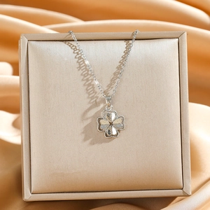 Silver four-leaf clover pendant necklace with textured clover on champagne silk background