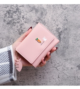 Handheld view of pink leather trifold wallet with rabbit print and fishbone charm