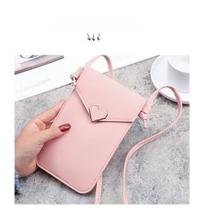 Dettaglio della borsa rosa in pelle per telefono con fibbia a cuore tenuta in mano