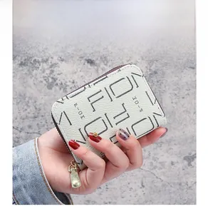 Détail d'un porte-cartes en cuir beige avec imprimé graphique et fermeture éclair dorée